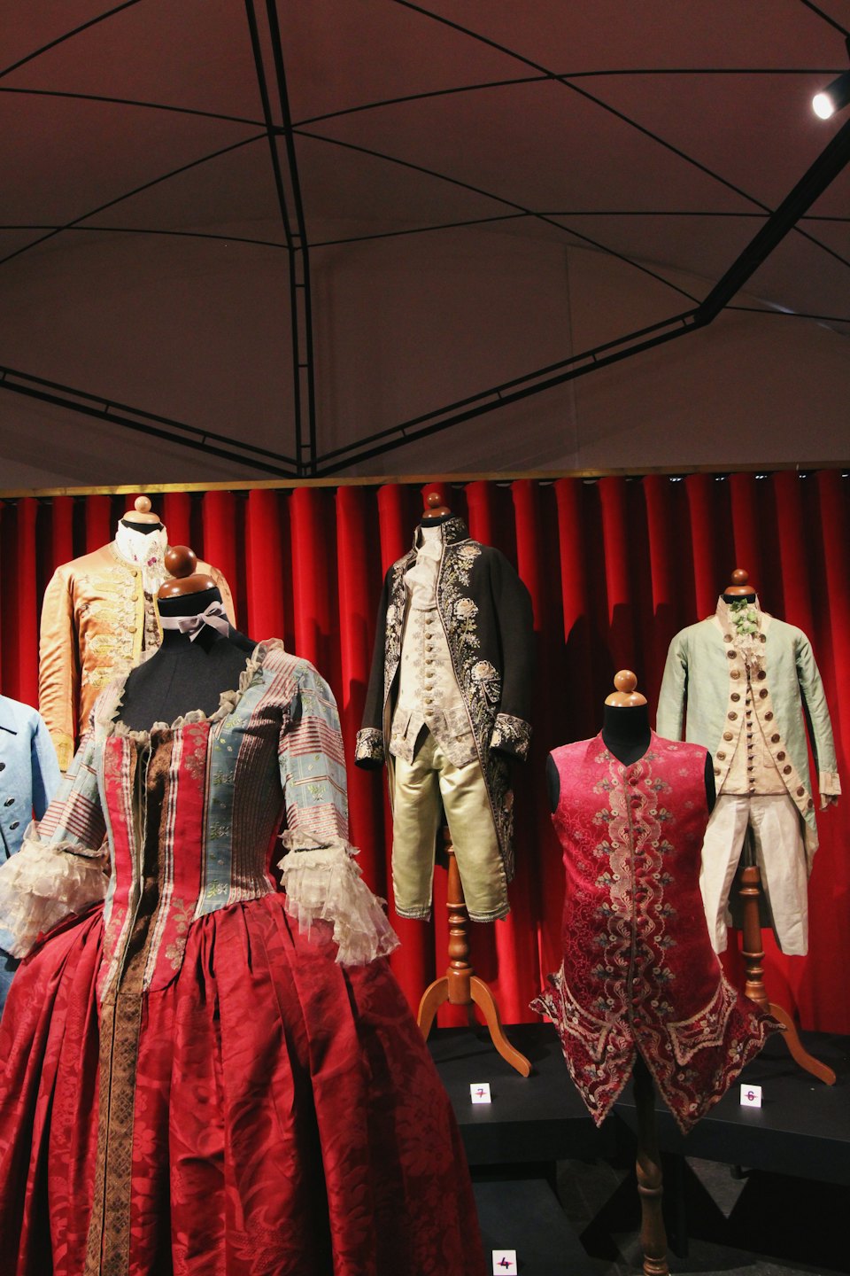 Costumi storici su manichini esposti davanti a tende rosse.