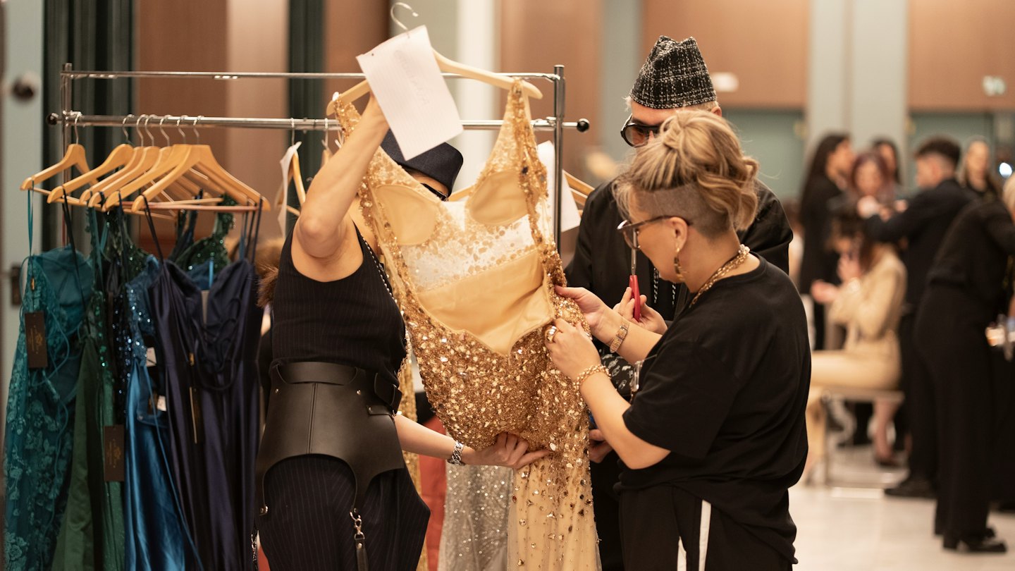 Professionisti che aggiustano un abito di paillettes dorate in uno studio di abbigliamento.