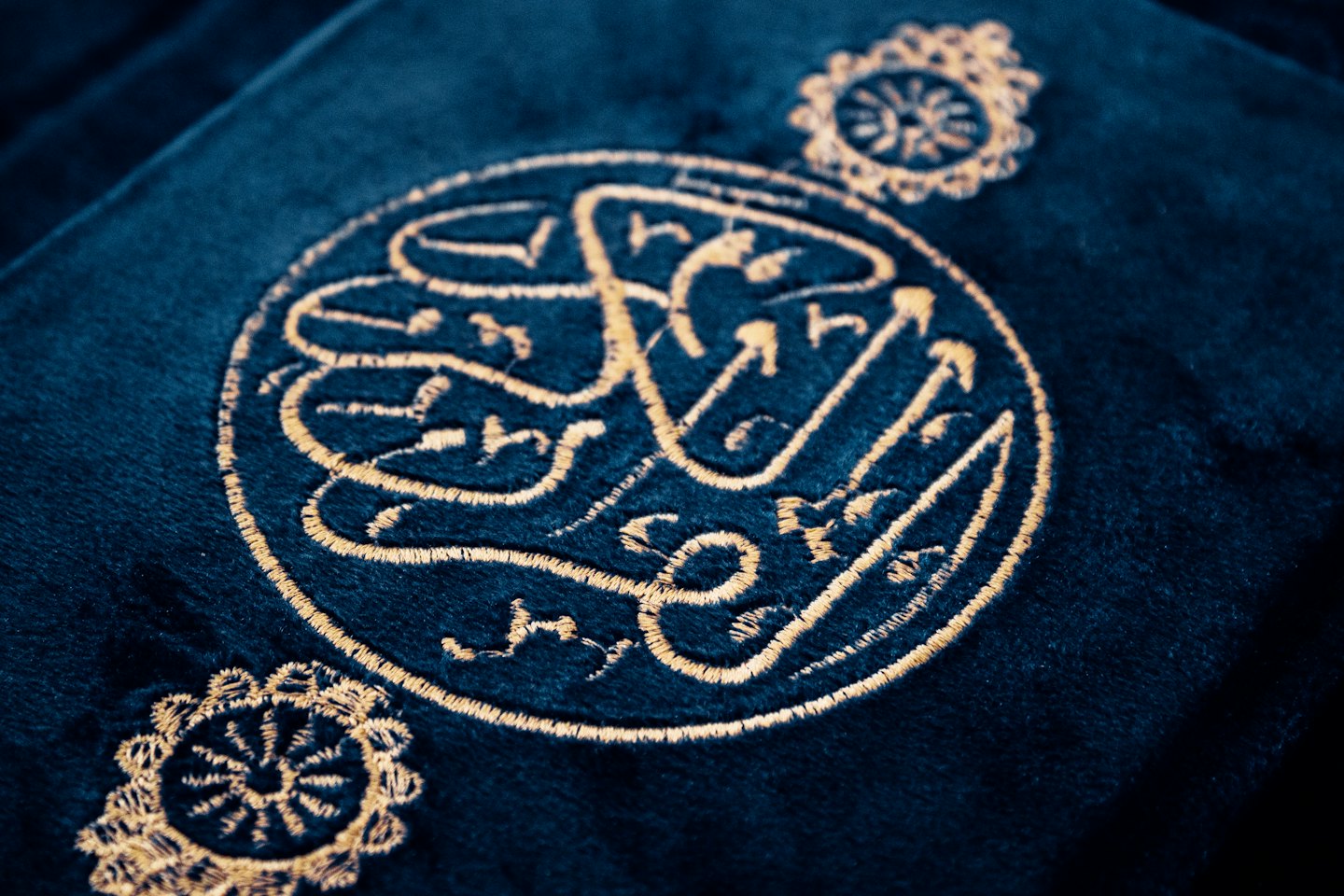 Tessuto blu scuro di velluto decorato con intricata calligrafia araba dorata.